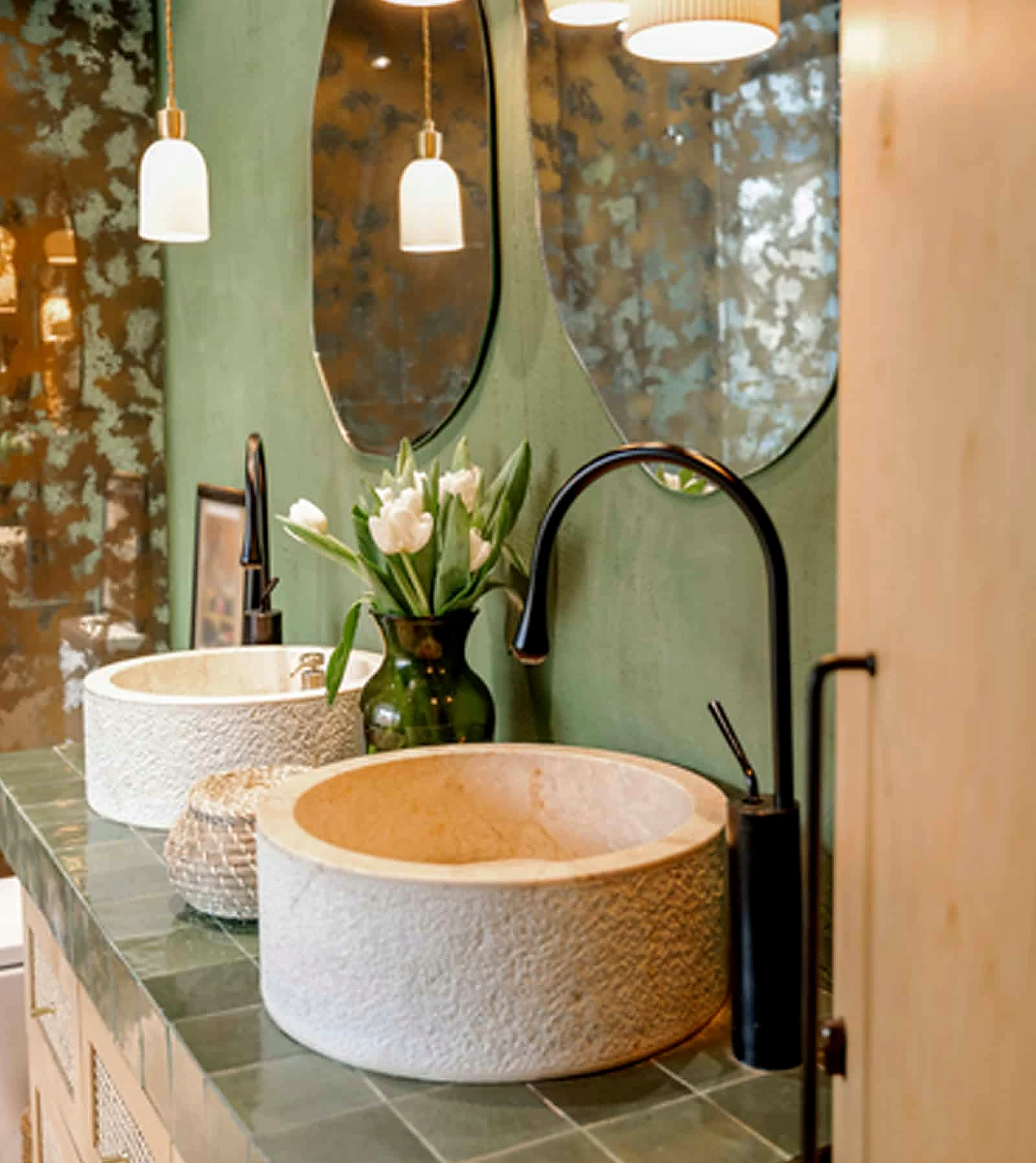 Green bathroom with sculptural stone vessel sinks and brass fixtures